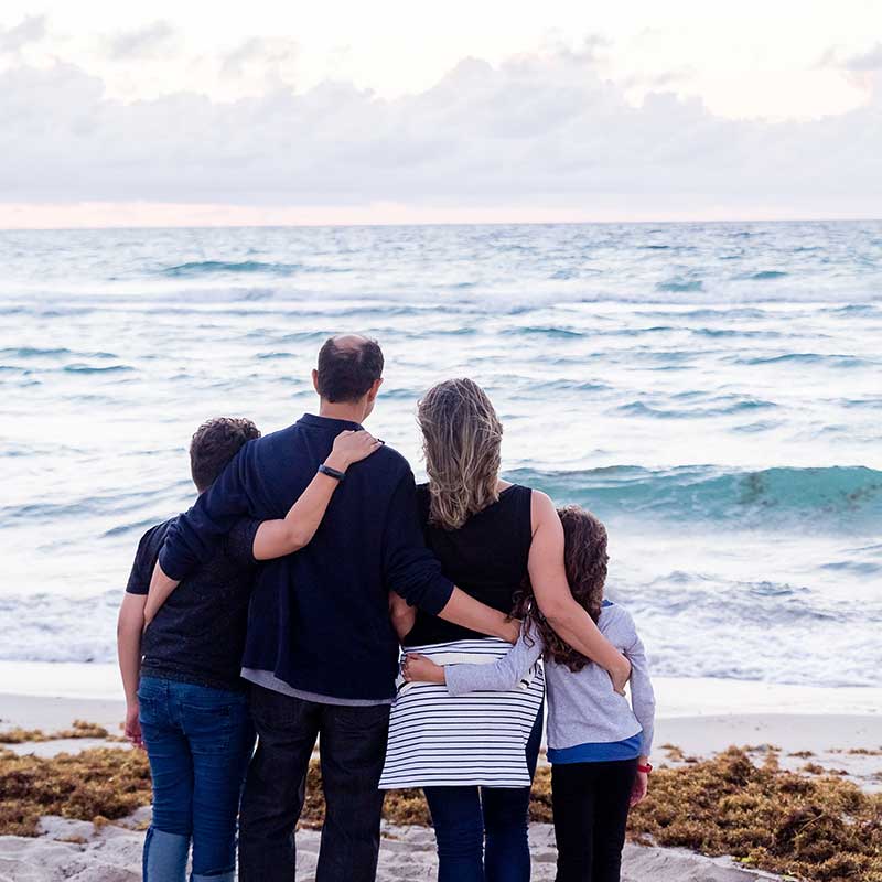 A family of father, mother, son and daughter gaze away from us across an ocean towards a sunset after a successful counselling session at Mudita